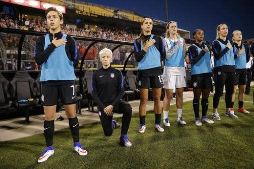 United States' Megan Rapinoe, second from left, kneels during the playing of the national anthem before the soccer match against Thailand, Thursday, Sept. 15, 2016 in Columbus, Ohio.  Rapinoe did not start the game against Thailand at Mapfre stadium. She knelt from a spot near the bench while the fellow reserves around her stood. 