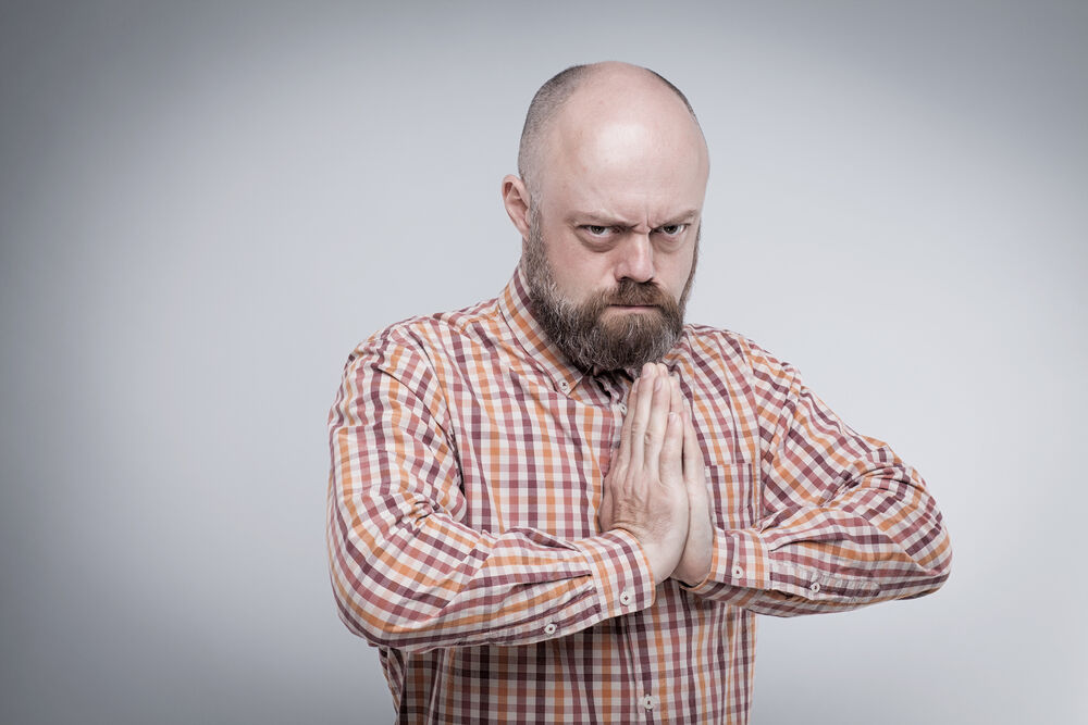 Angry man staring at camera with hands folded in prayer