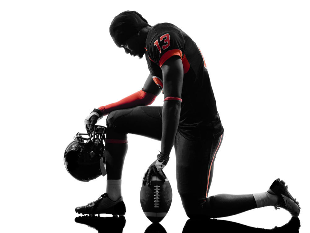 A football player takes a knee before the game