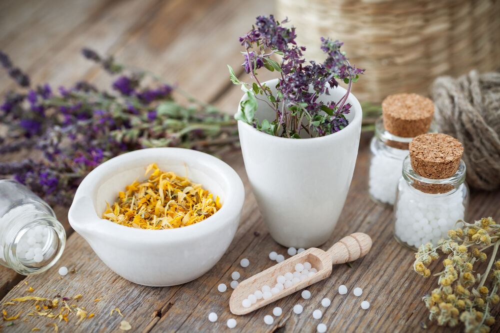 Mortar and bowl of dried healing herbs and bottles of homeopathic globules.