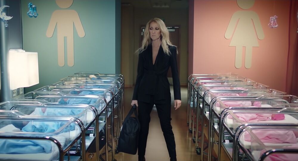 Celine Dion standing in front of babies dressed in pink or blue.