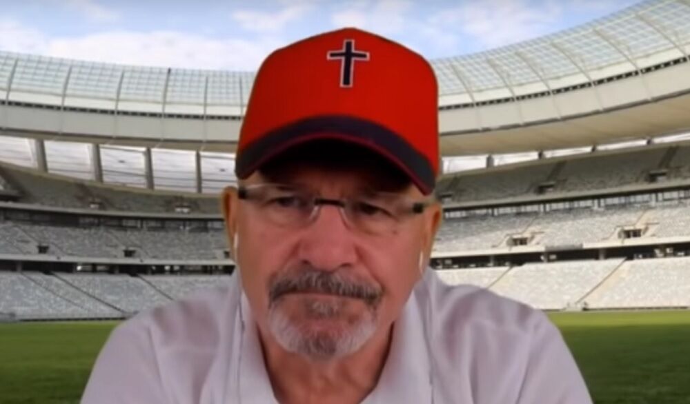 A man in a red cap with a cross. The background is a computer generated image of a stadium.
