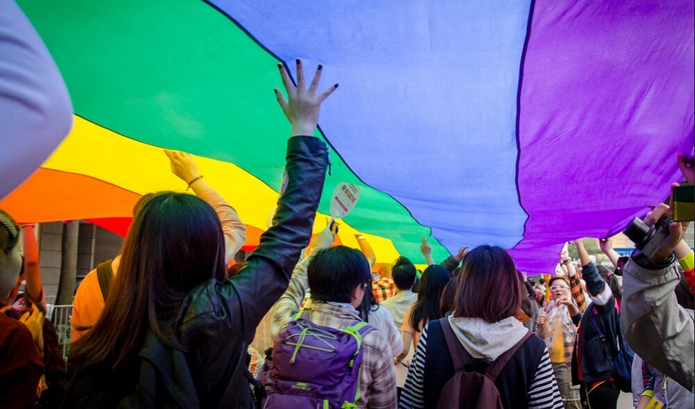 Backs of people marching and holding a rainbow banner