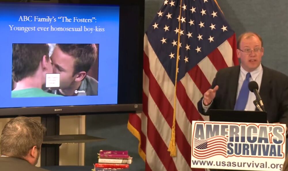 Peter LaBarbera at a lecturn with an American flag behind him. Next to him is an image of two men kissing, partly censored.