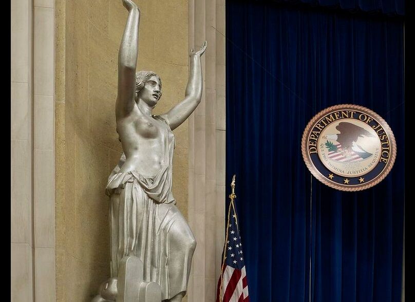 An aluminum statue of Justice showing one breast, next to the Department of Justice seal