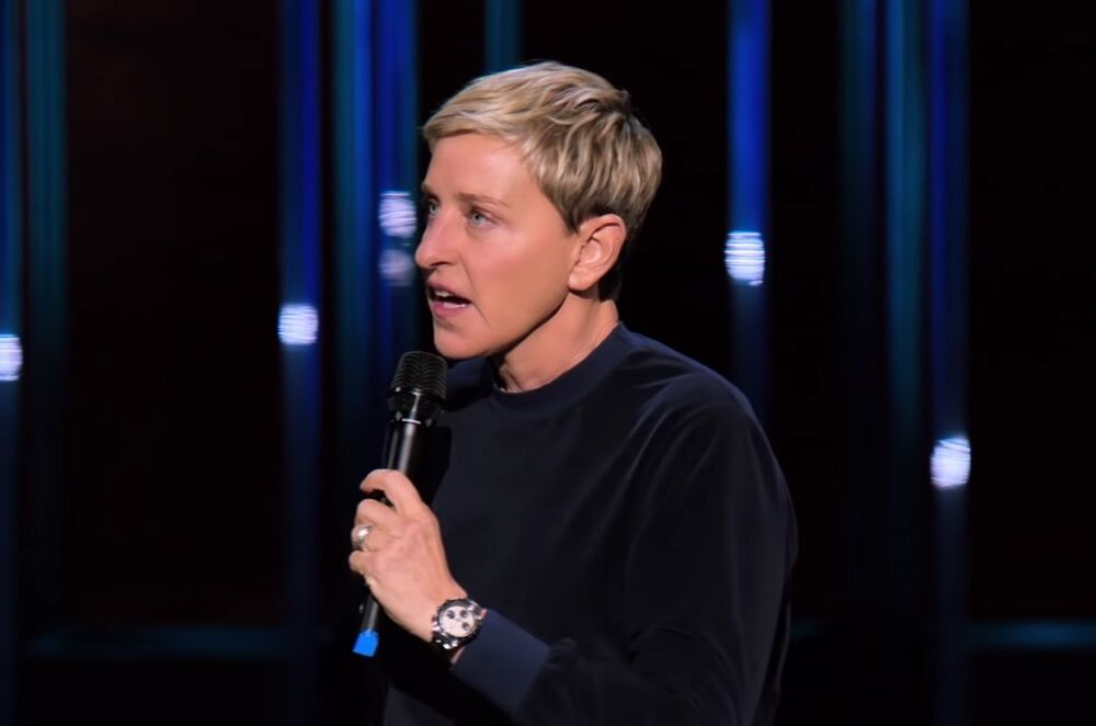 Ellen in a black sweater holding a microphone.