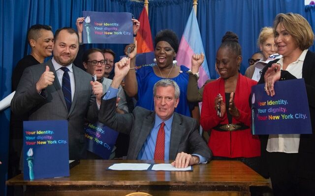 Bill de Blasio sitting, surrounded by people who are cheering.