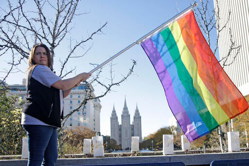 In this Nov. 14, 2015, photo, Sandy Newcomb poses for a photograph with a rainbow flag as Mormons gather for a mass resignation from the Church of Jesus Christ of Latter-day Saints, in Salt Lake City.