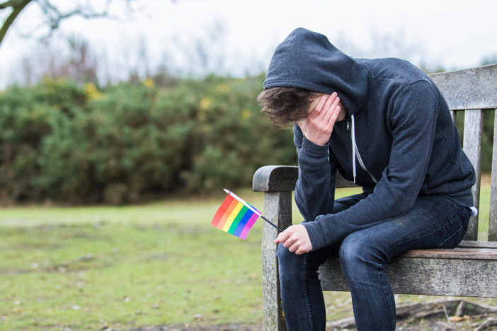 A teen crying with a rainbow flag, signifying gay LGBTQ bisexual lesbian transgender queer bullying discrimination in schools