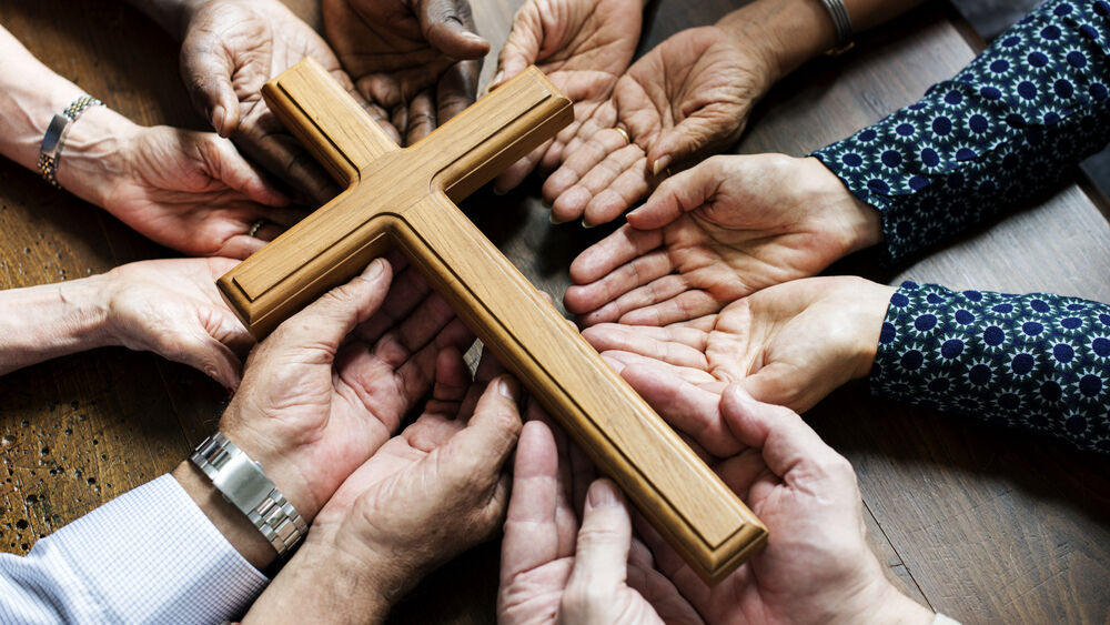 Group of christianity people pray together by using their hands to hold up a medium-sized cross.