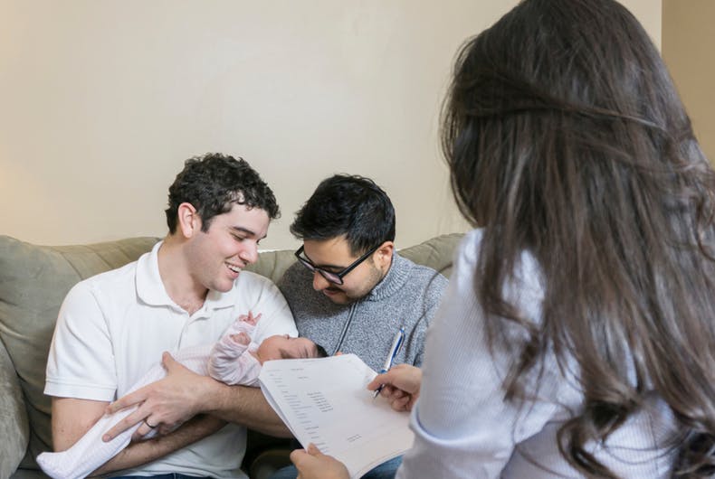 A gay couple with a baby and a functionary with a checklist monitoring them