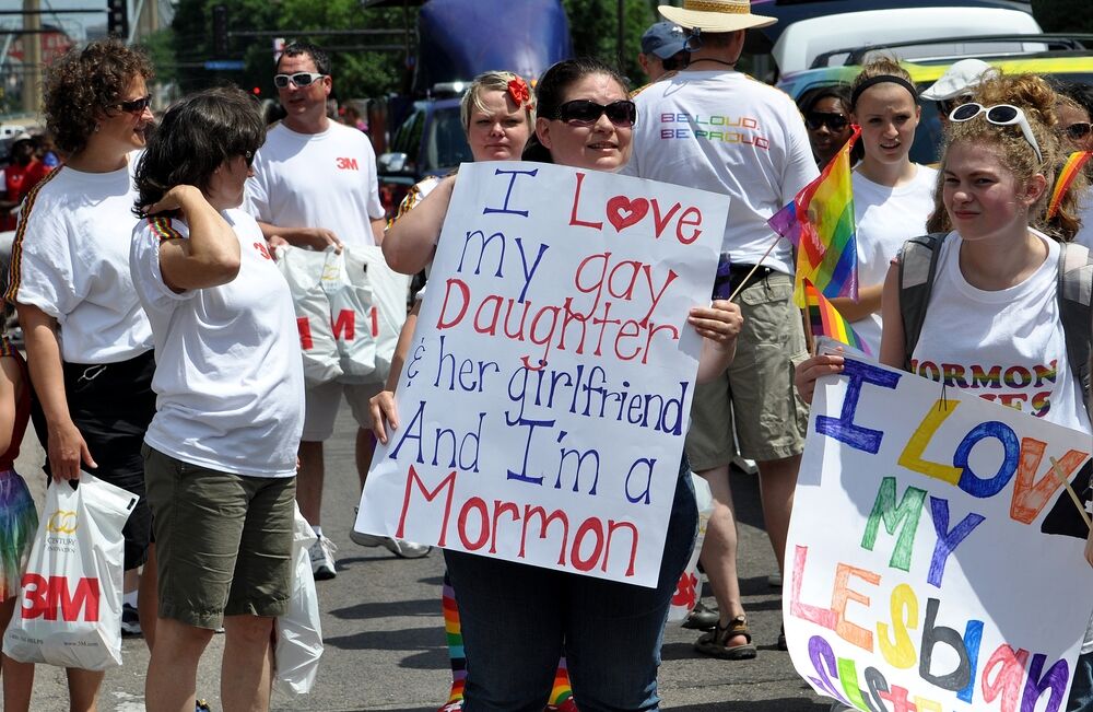 Woman holding a sign that says "I love my gay daughter & her girlfriend And I'm a Mormon"