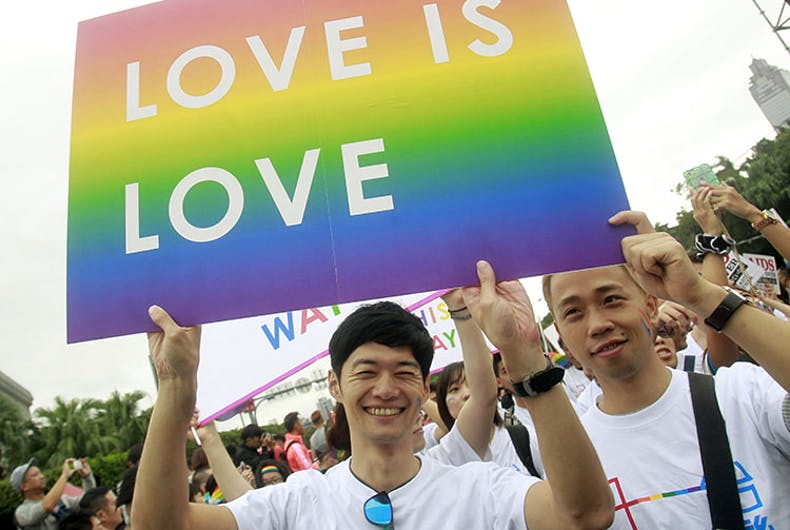 Two people in white T-shirts holding up a "Love is love" sign.