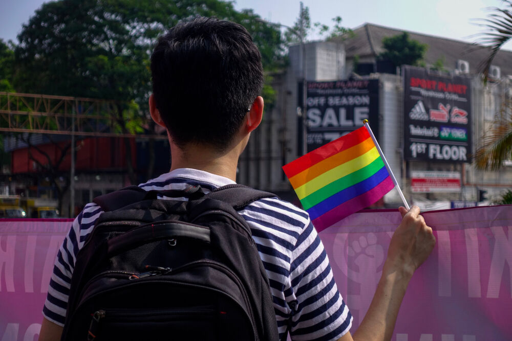 A young man quietly waves a small rainbow flag at #WomensMarchMY in conjunction with International Women’s Day 2019