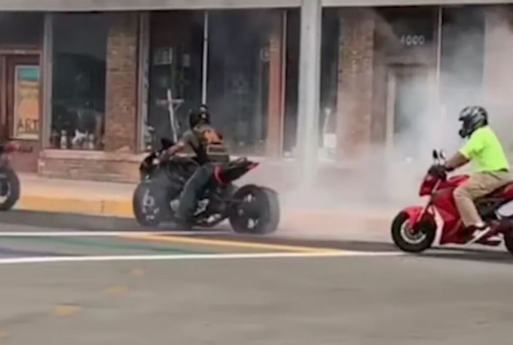 A motorcycle produces a lot of smoke on the rainbow crosswalk