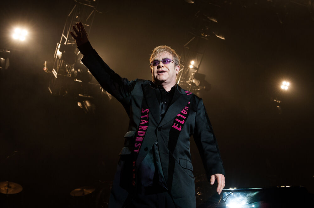 Elton John waves at a concert.