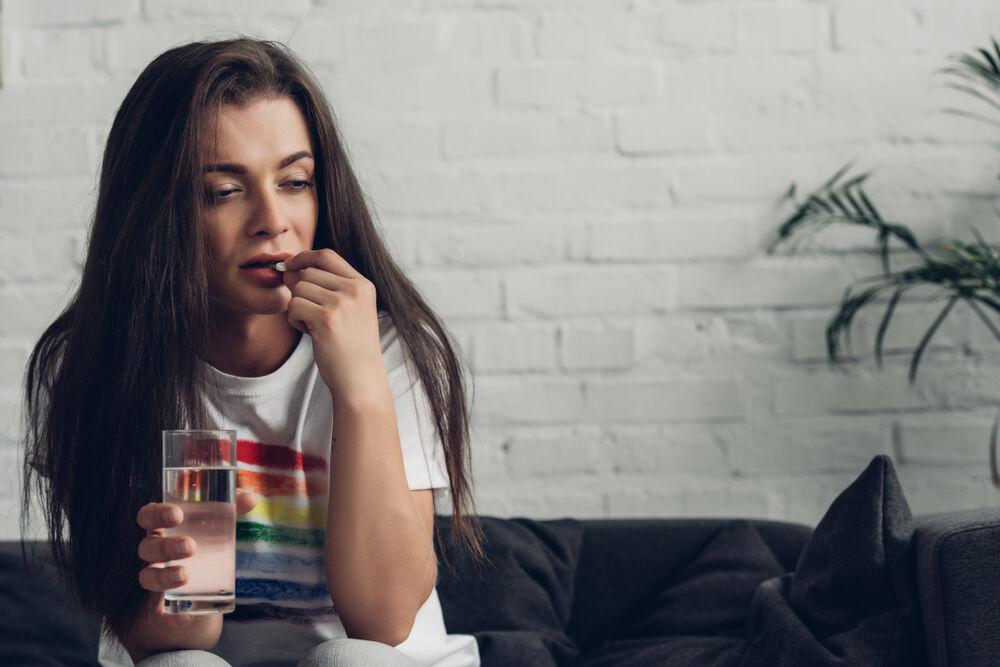depressed young transgender woman taking pill on couch