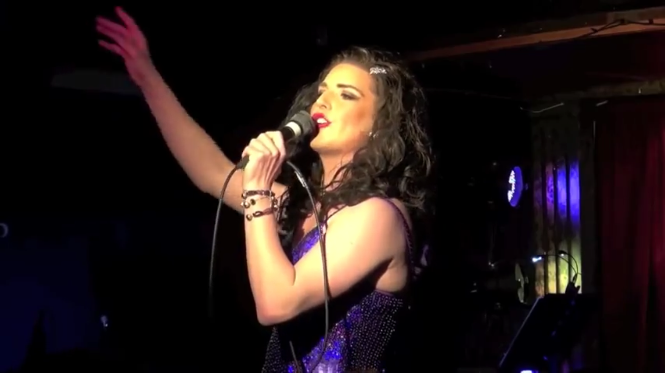 UK Cabaret entertainer Topsie Redfern singing into a microphone on a stage.