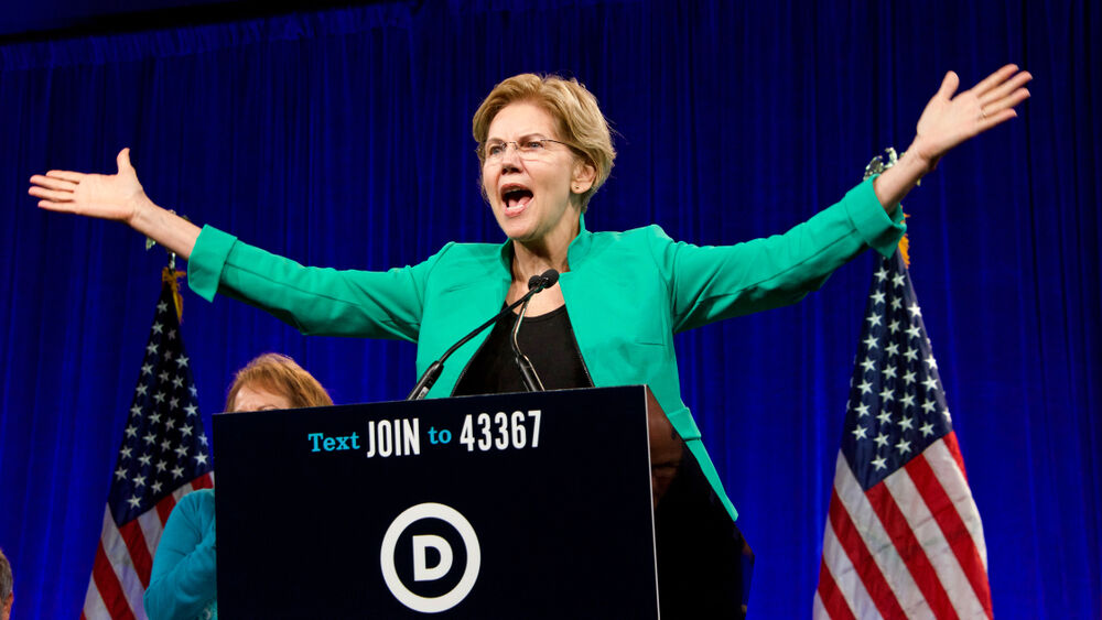 Elizabeth Warren wears a blue blazer while speaking at a lectern onstage.