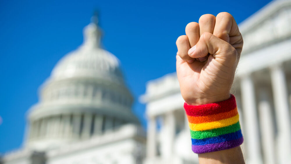 Hand wearing gay pride rainbow wristband making a power fist gesture in front of the US Capitol Building in Washington, DC, USA