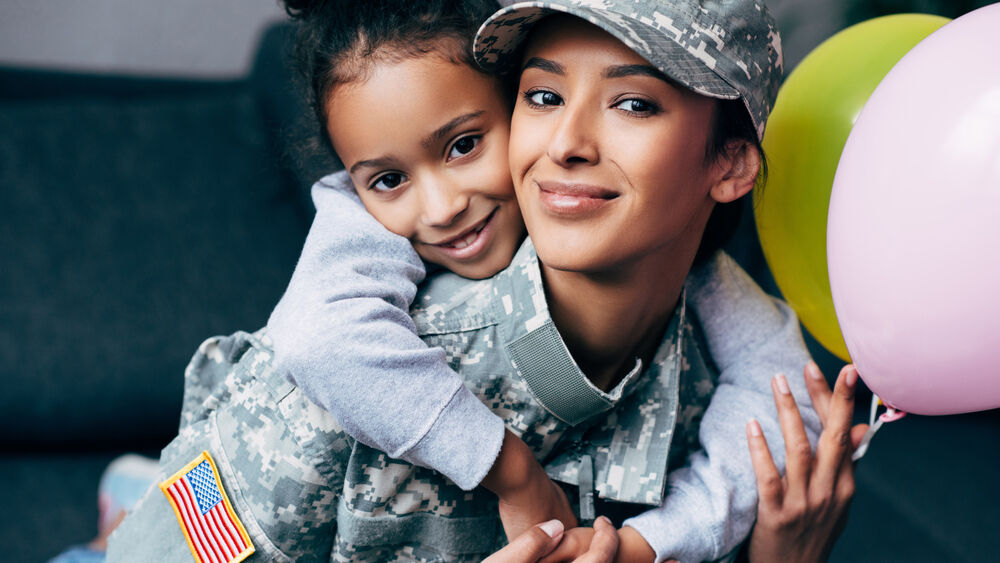 African american daughter hugging her mother in military uniform with balloons at home