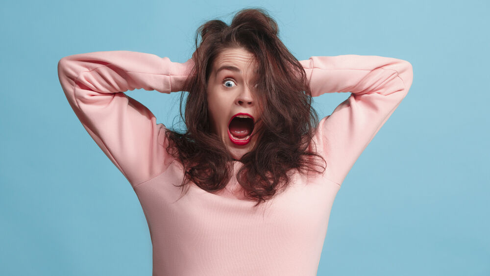 The screaming woman with horror expression. Beautiful female half-length portrait isolated on blue studio backgroud. The crazy woman.