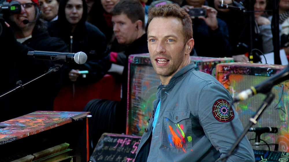 Chris Martin, the leader singer of Coldplay, plays a rainbow colored piano