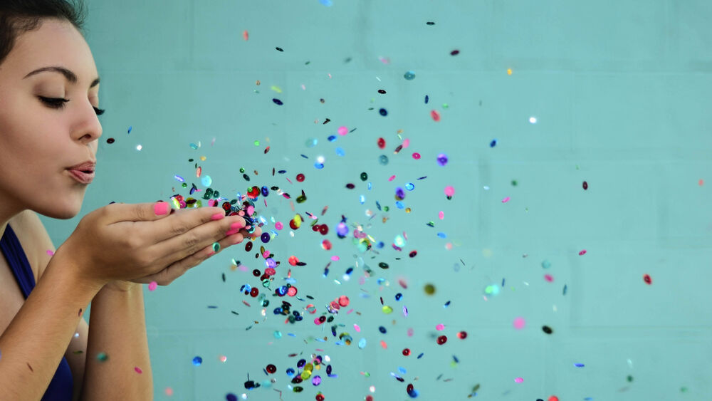 young woman blowing glitter in sports bra on blue background