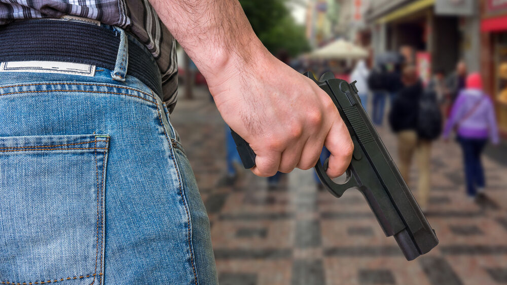 a man holds a gun while at a crowded shopping area.