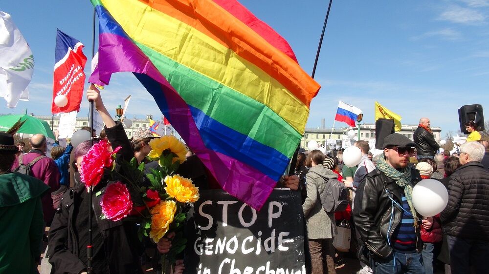 Protestors with a rainbow flag and a sign that says "Stop genocide in Chechnya"