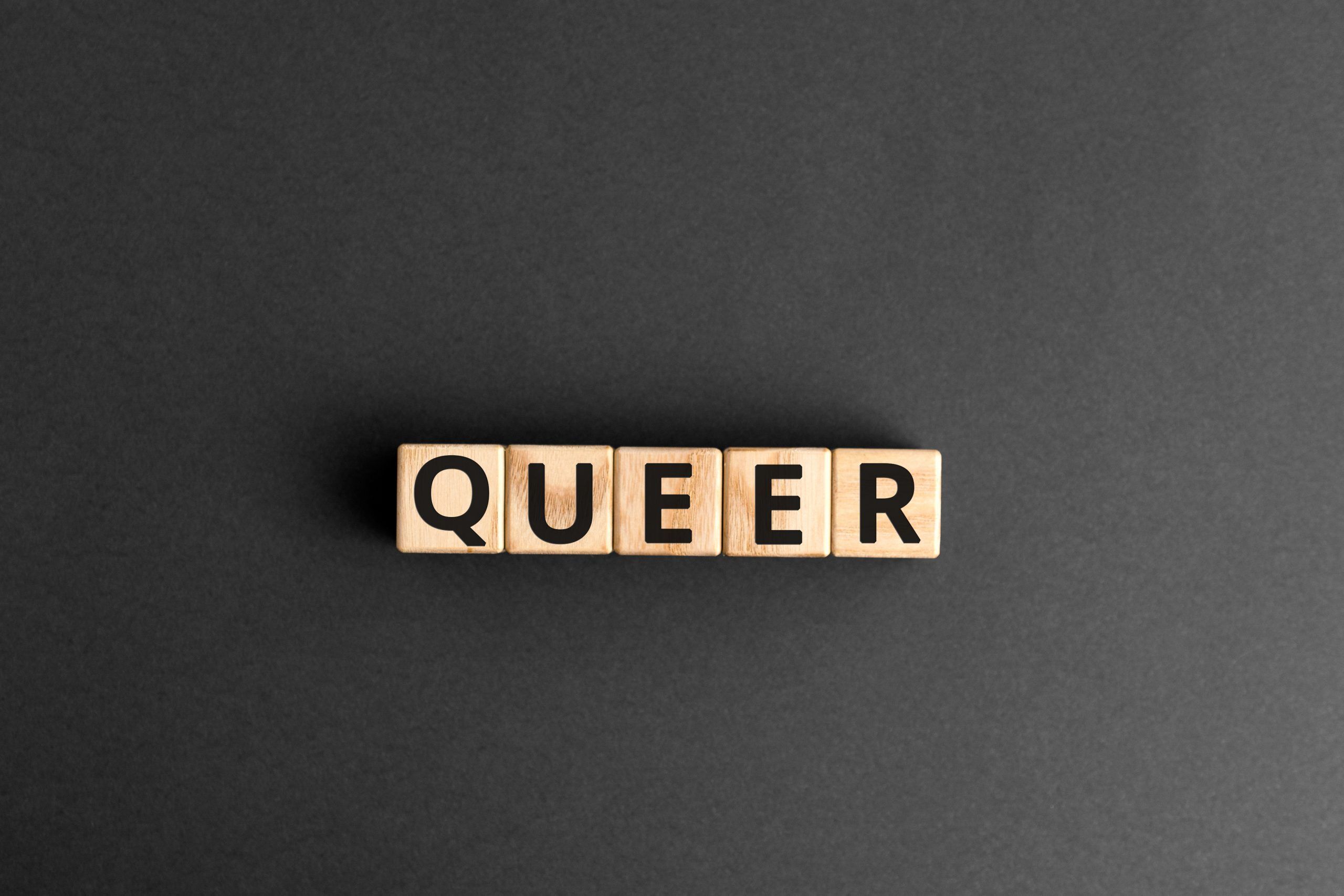 Queer - word from wooden blocks with letters, queer concept, random letters around, top view gray background