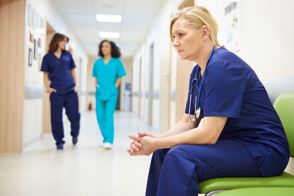 A doctor looks forlorn while two other medical staff talk behind her. Maybe she was the victim of anti-LGBTQ patient harassment?