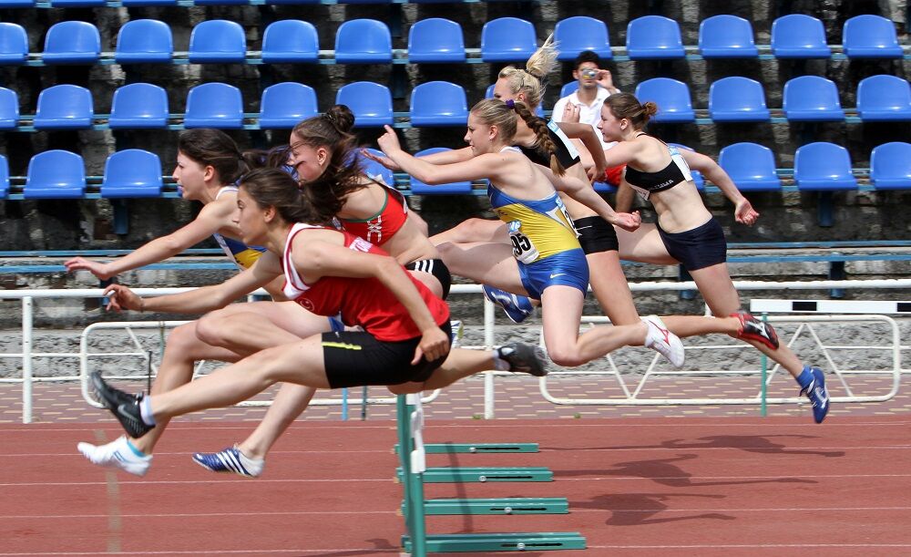 High school girls jumping over a hurdle at a track meet