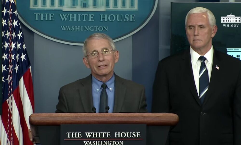 Anthony Fauci speaking at a lecturn while Mike Pence glares over his shoulder