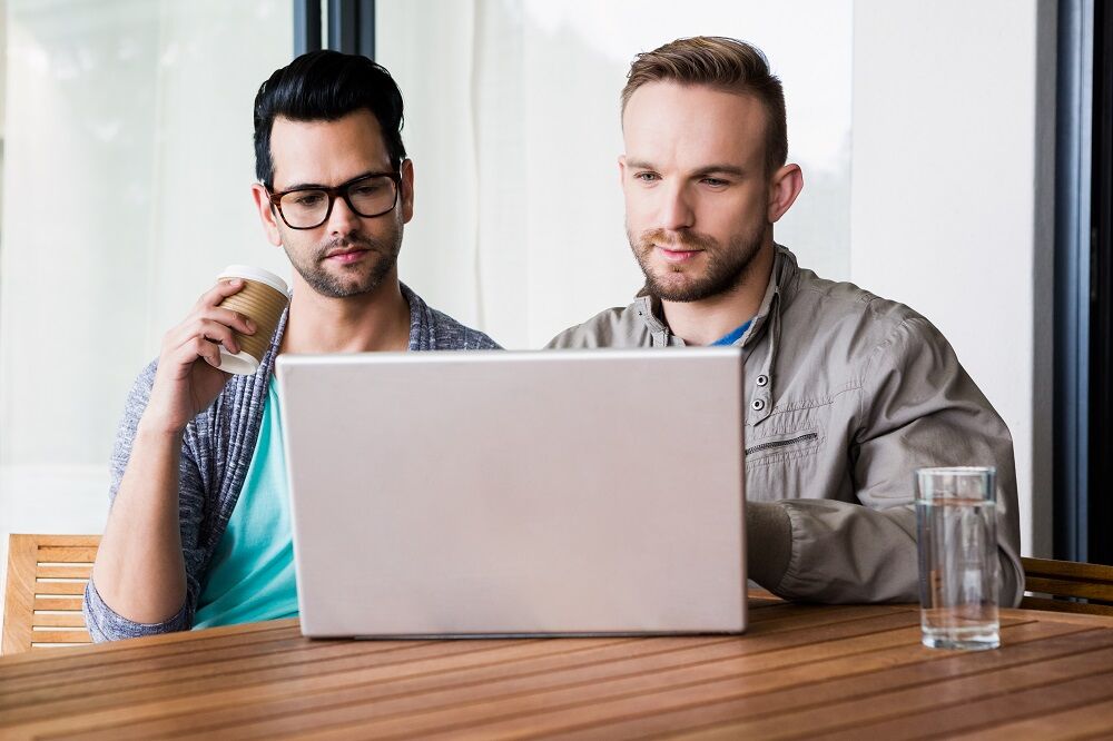 A gay couple looking at a computer. They are not smiling.