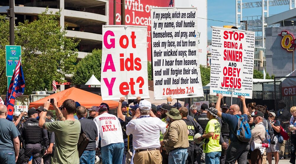 Protestors with anti-LGBTQ signs. One says "GAY: Got AIDS Yet?" and another says to "Obey Jesus"