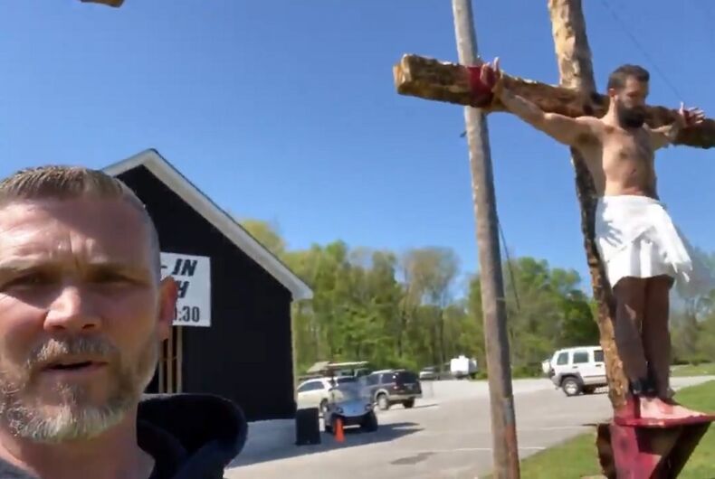 Greg Lock standing in front of a cross with a person on it. The person is standing on a ledge.