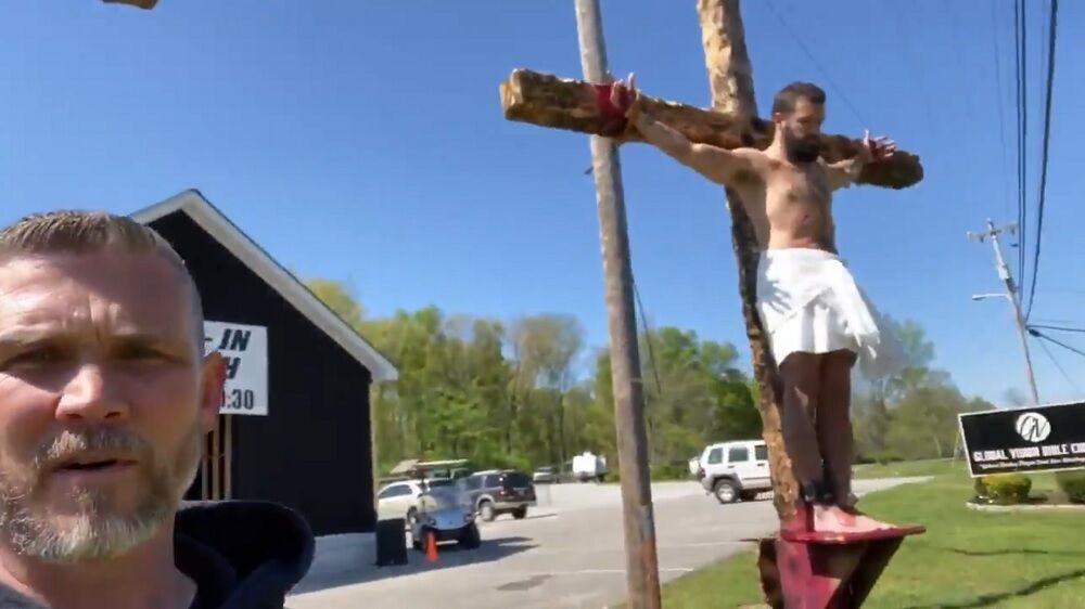 Greg Lock standing in front of a cross with a person on it. The person is standing on a ledge.