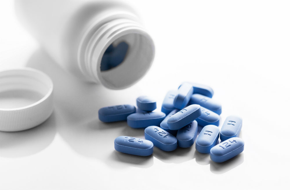 Truvada PrEP medication pills, which are blue, on a white table next to a bottle.