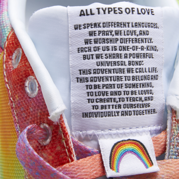 A closeup photo of one of Reebok's new Pride-Inspired rainbow sneakers, with the tongue of the show saying "All Types of Love" with a full manifesto about the shoe line below it.