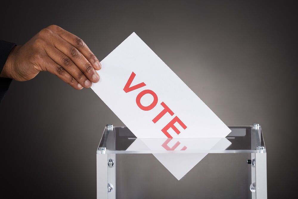 A hand putting a card marked "vote" into a ballot box