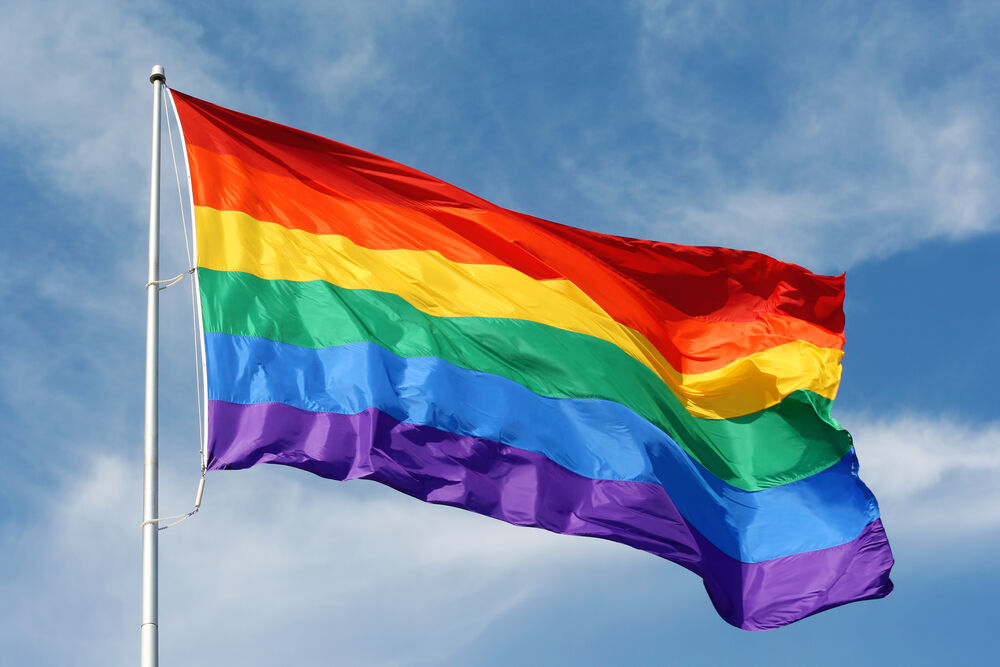 Pride flag flying against a blue sky