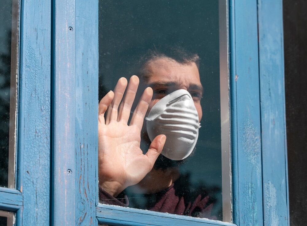 A person with a facemask pressing their hand against a window. They want out, y'all.