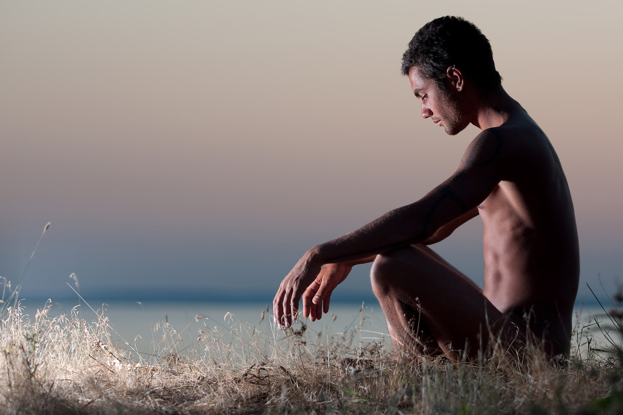 Nude man sitting on the shore of the ocean