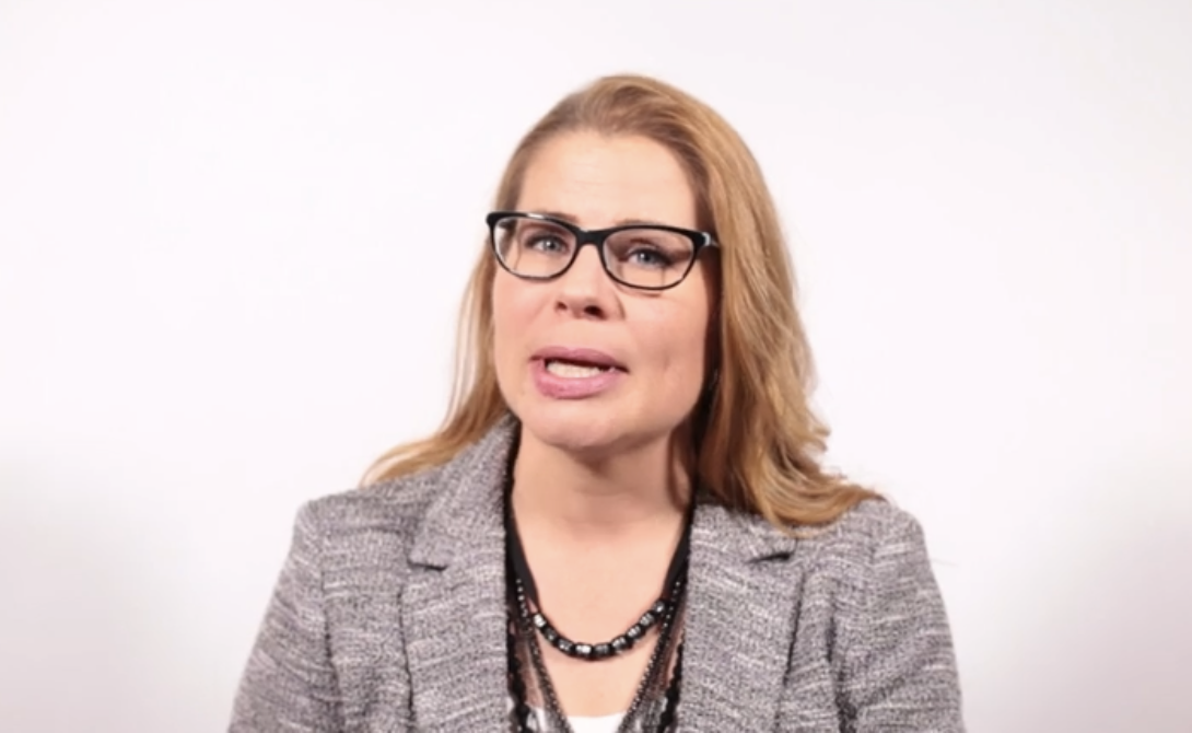 Sarah Parshall Perry, with brunette hair, wearing Black glasses and a grey blazer