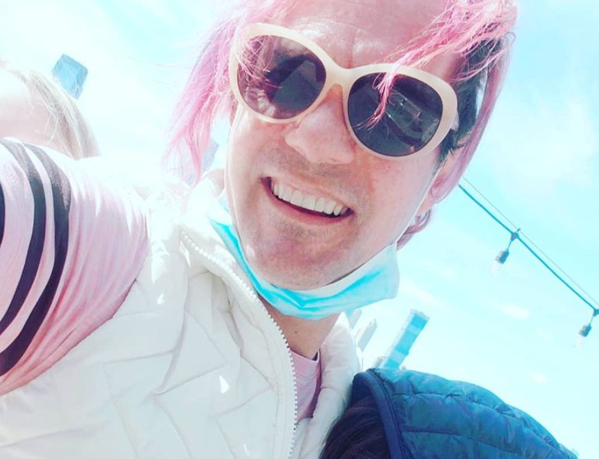 A headshot of Andrea Breanna, trans founder of RebelMouse, with pink hair and a blue mask in the sun.