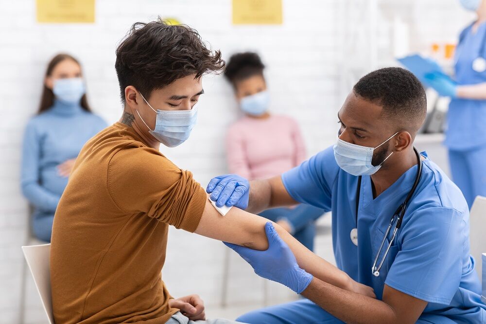 A doctor with a facemask gives a vaccine to a patient with a mask