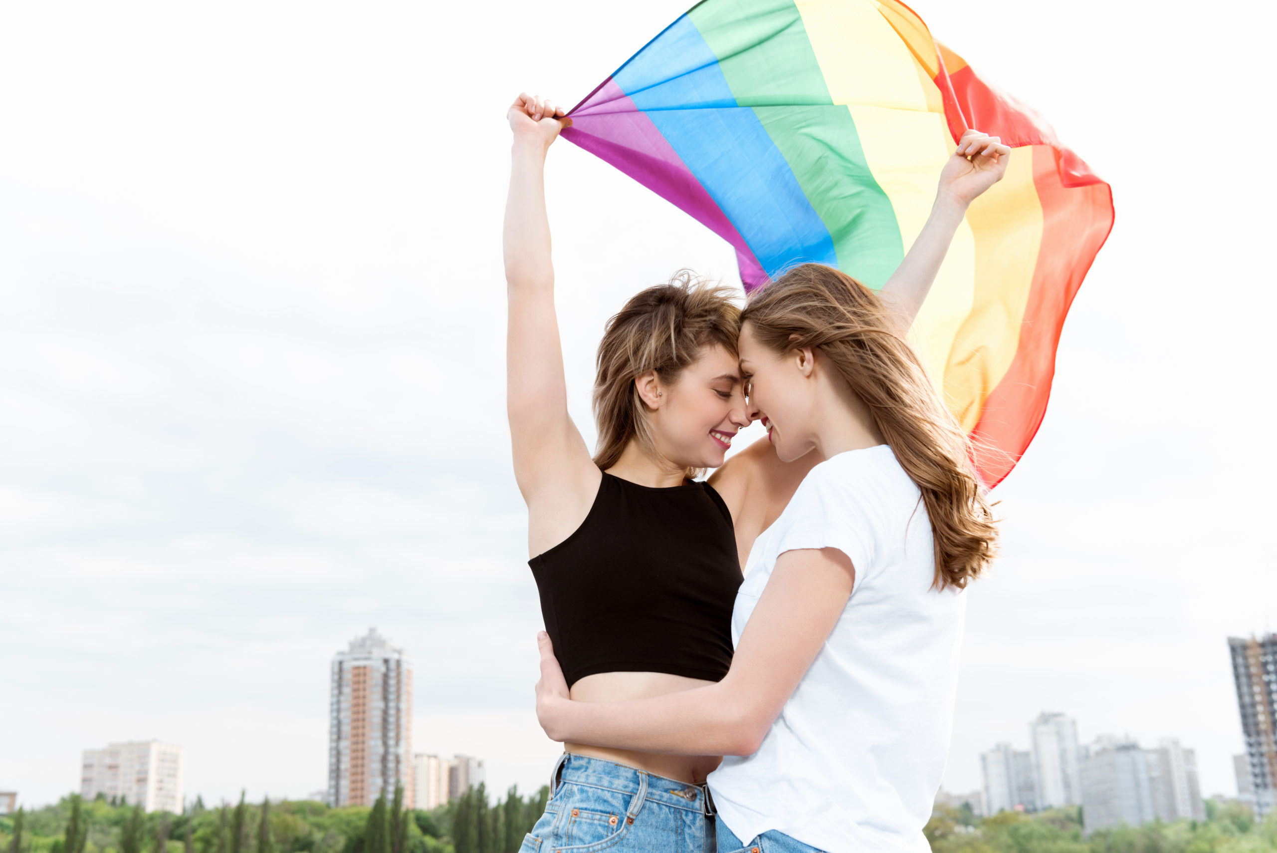 young sensual lesbian couple embracing and waving lgbt flag outdoors
