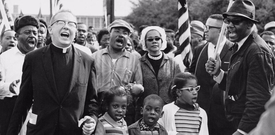 The black and white photo is of the Abernathy Family marching with Martin Luther King and Coretta Scott King on Day 4 of the Selma to Montgomery March for the Right to Vote.
