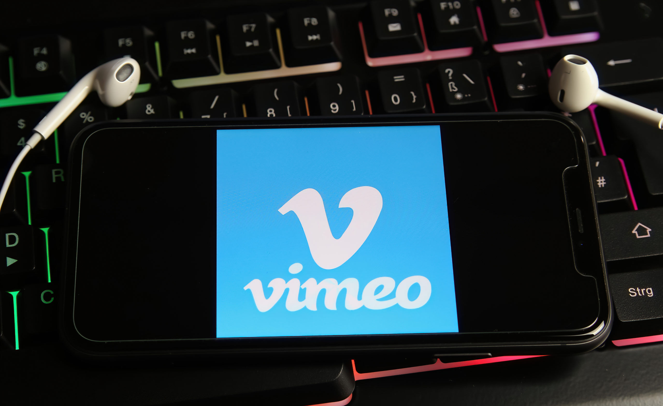 Viersen, Germany - February 9. 2021: Closeup of smartphone screen with logo lettering of video live streaming platform vimeo on computer keyboard (focus on letter V in center)
